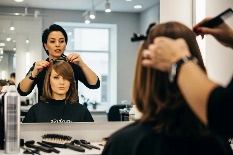 A professional hairstylist adjusting a model’s bangs in a salon mirror.
