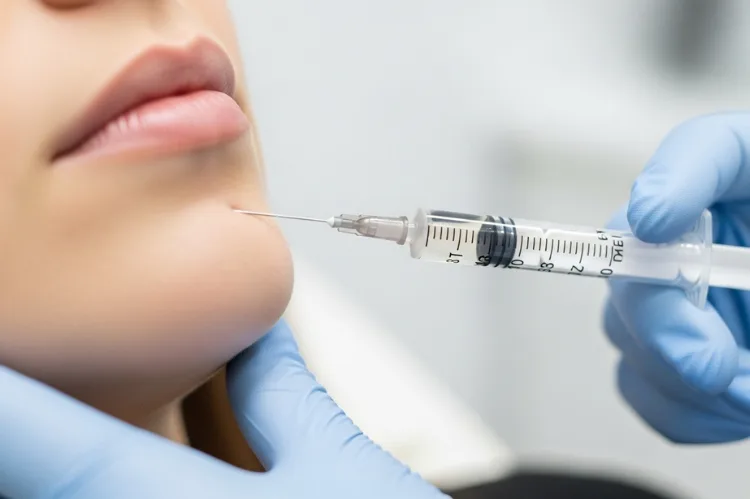 Close-up of filler syringe near chin gloved hands.
